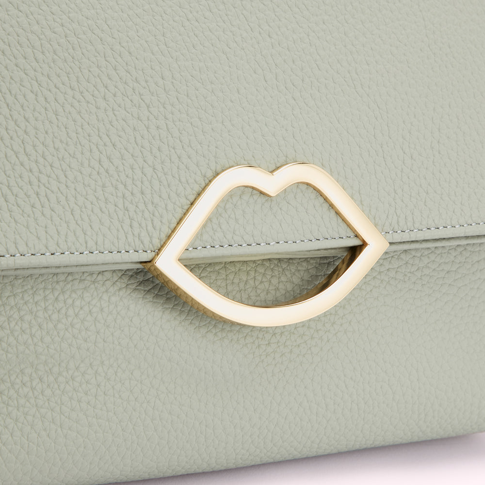 Close-up of a sage green textured leather purse with a gold lip-shaped clasp.

