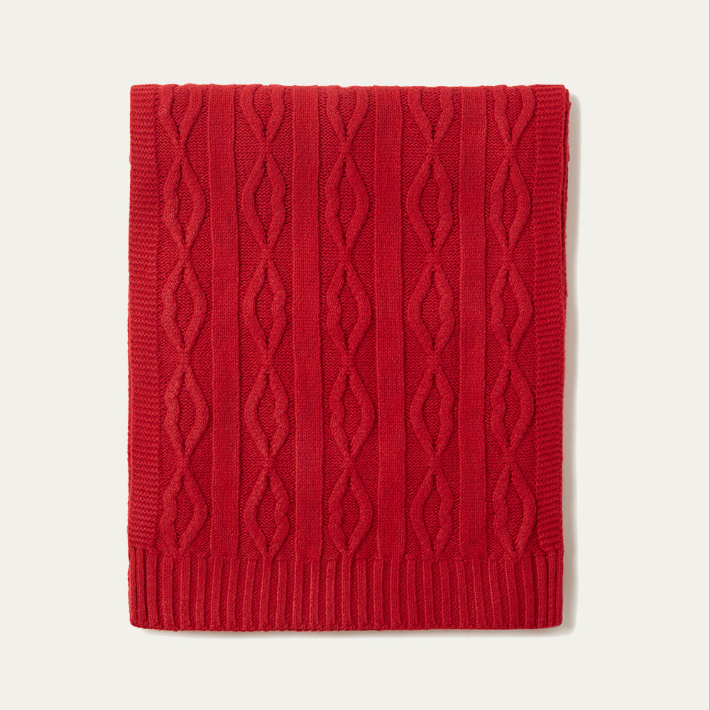 A red lip cable knit throw folded on a beige background