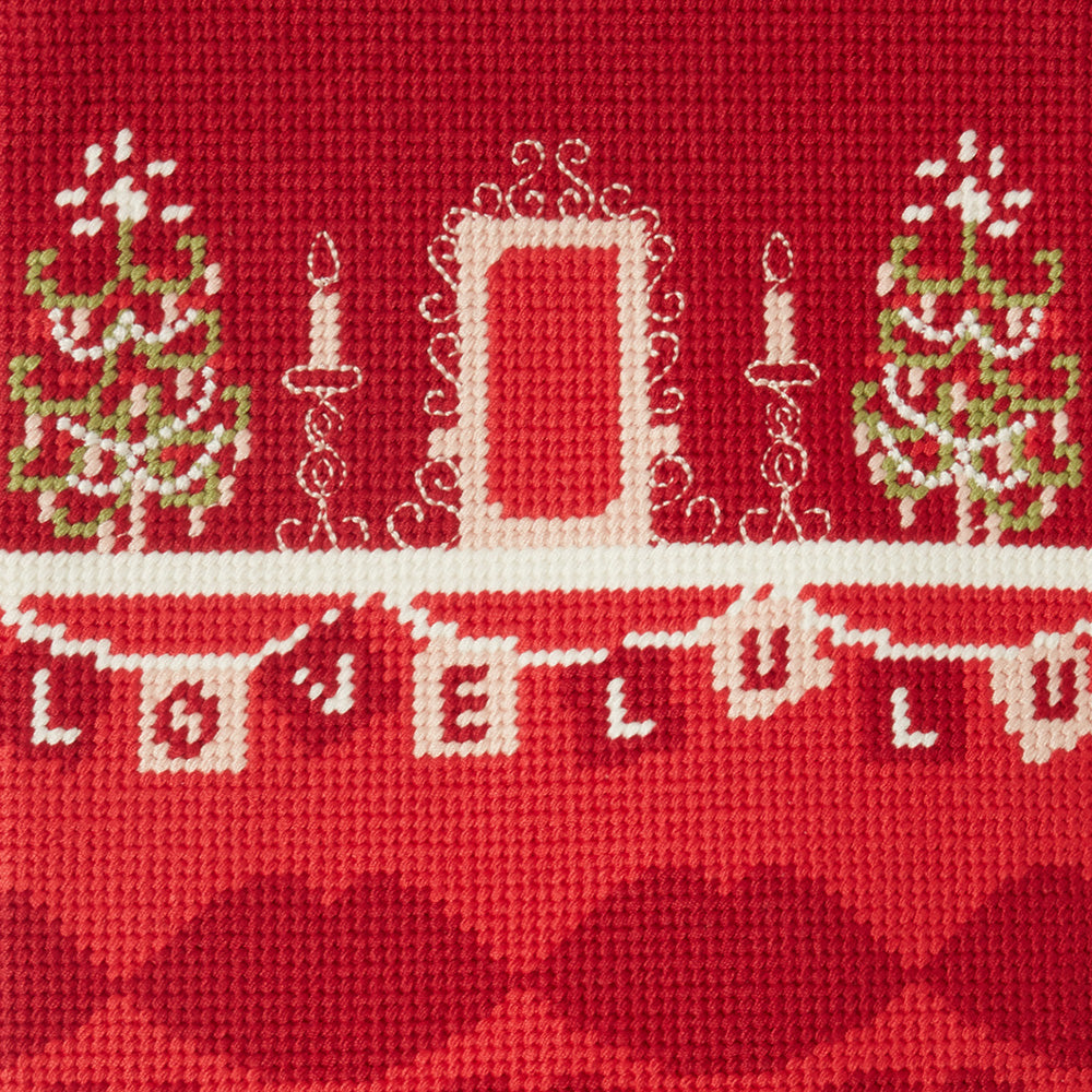 Cross-stitched design on a Christmas stocking of a fireplace scene with trees, a house, and bunting reading 'Love Lulu'.