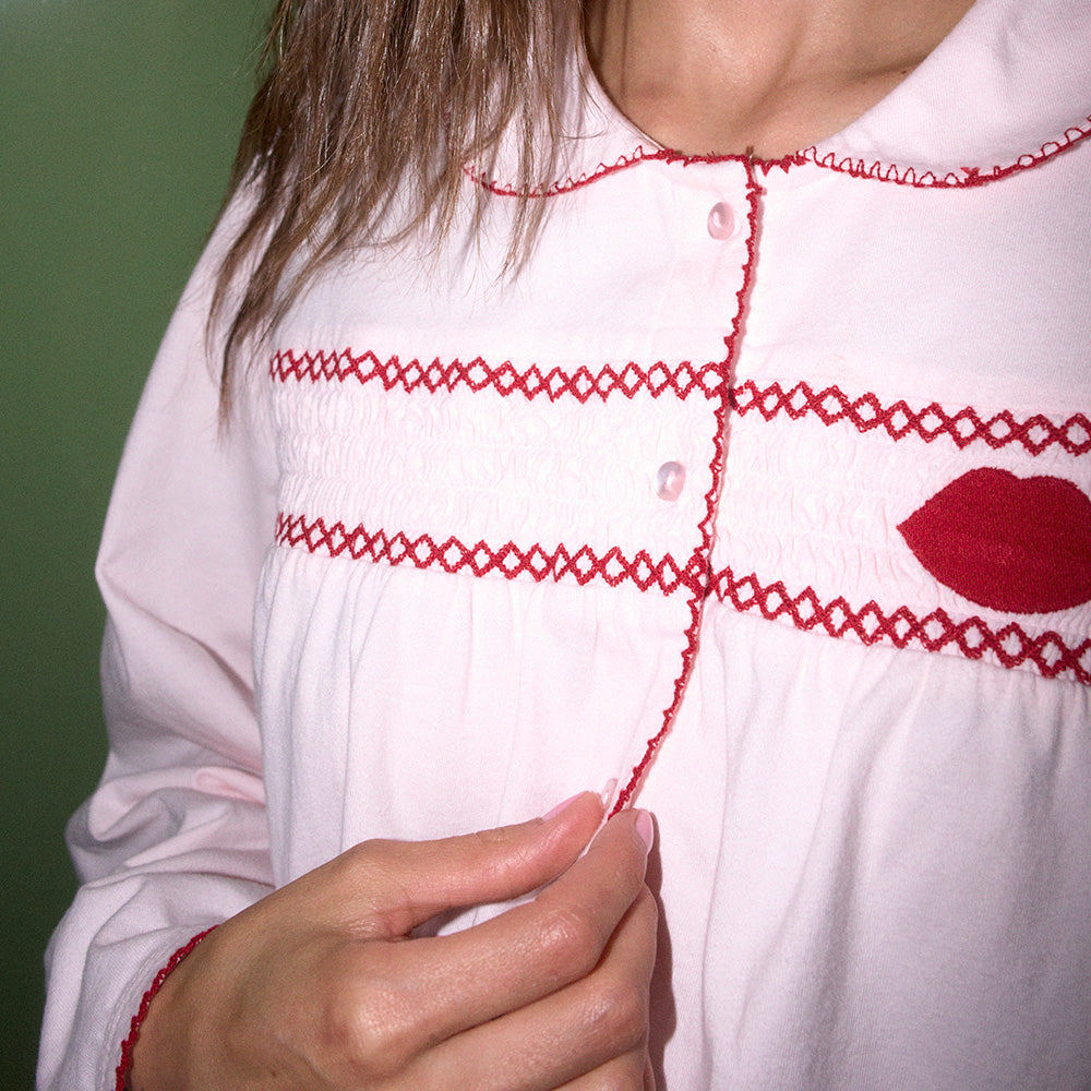 Close up of pale pink pyjama shirt with red embroidery worn by a person against a green background