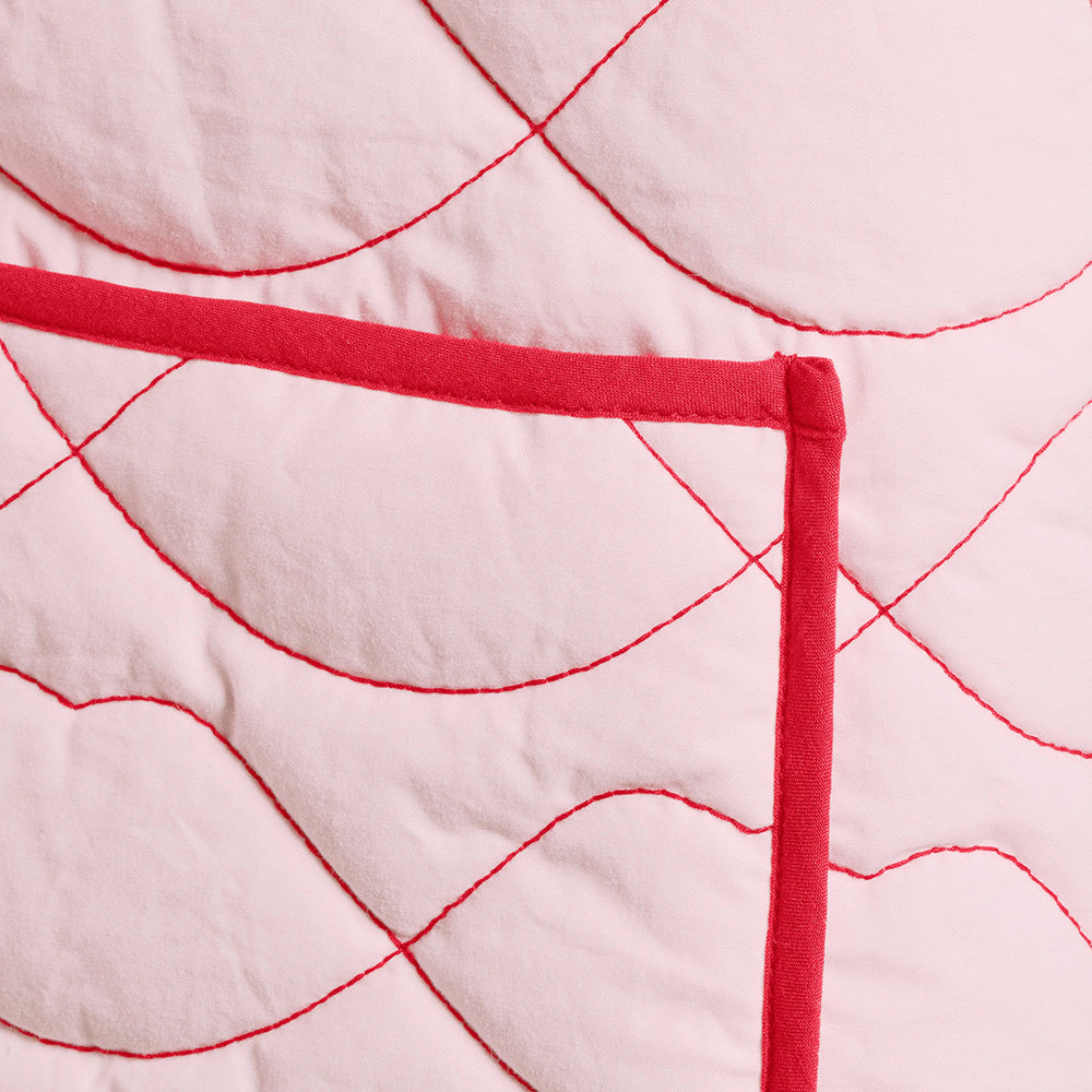 Close-up of a quilted jacket with red  lip shaped stitching on a light pink background