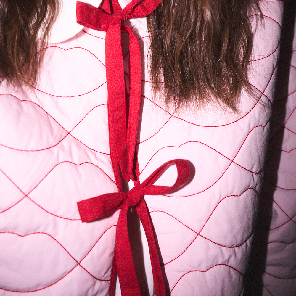 Close-up of a pink quilted jacket with lip shaped quilting and a red ribbon tie in the center.