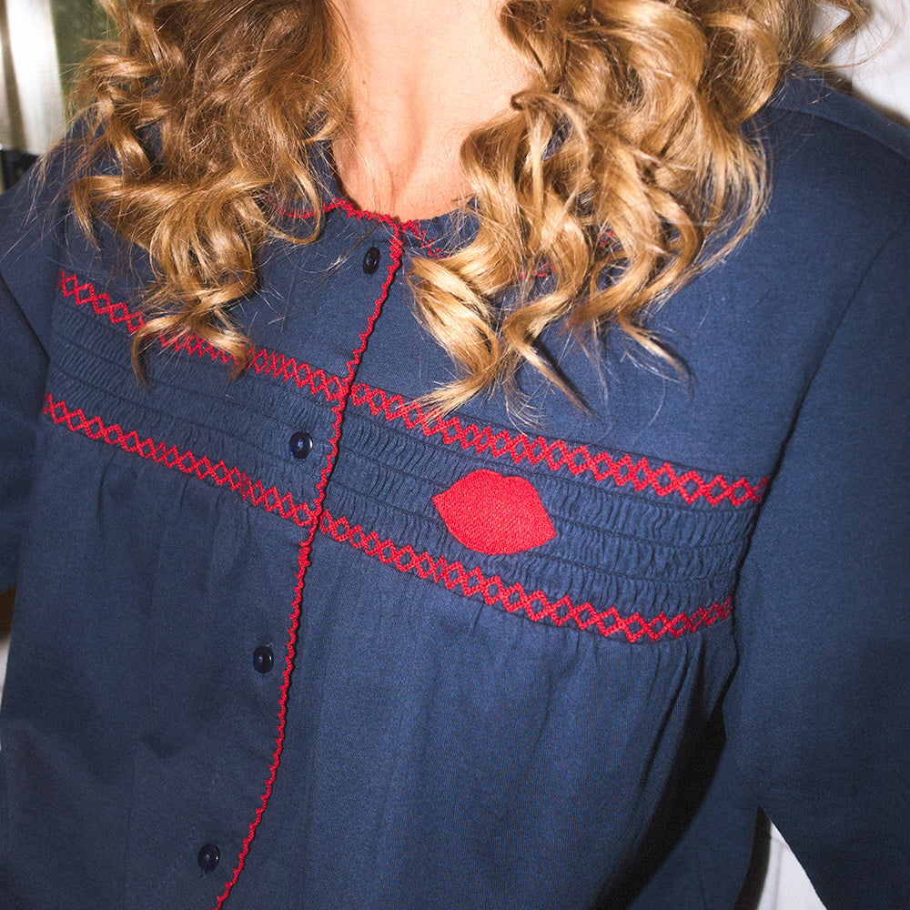 Close-up of a navy pyjama shirt with red stitching and a red embroidered lip on the front.