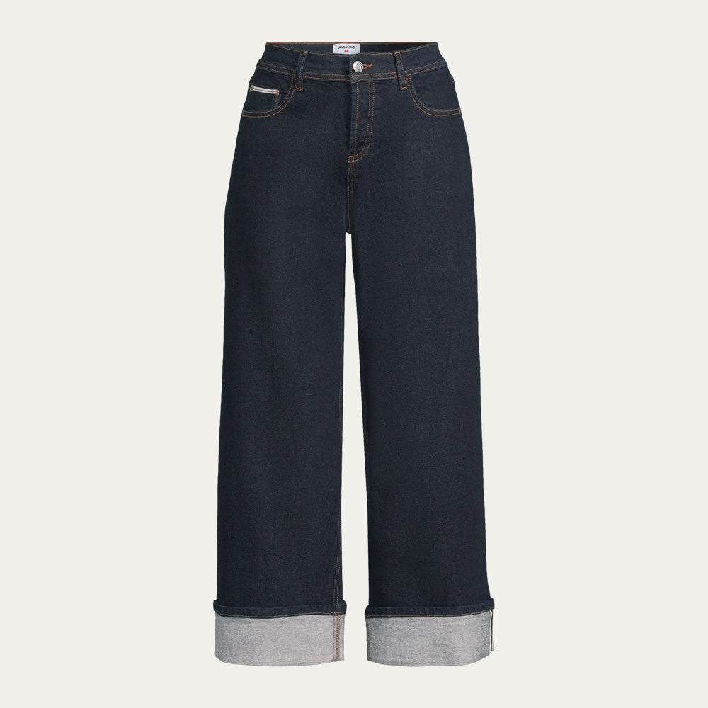 Dark denim jeans with turned up cuffs on a beige background.