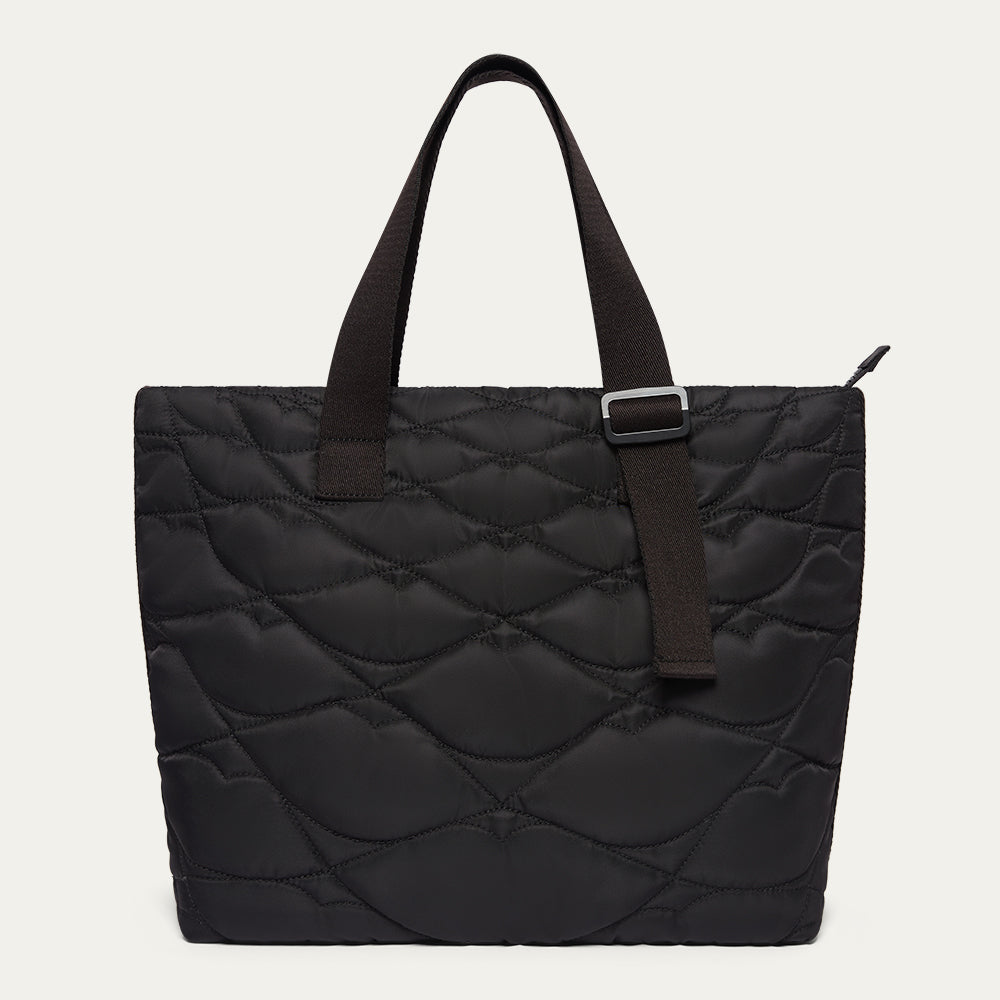 Black quilted tote bag with black woven straps on a light gray background