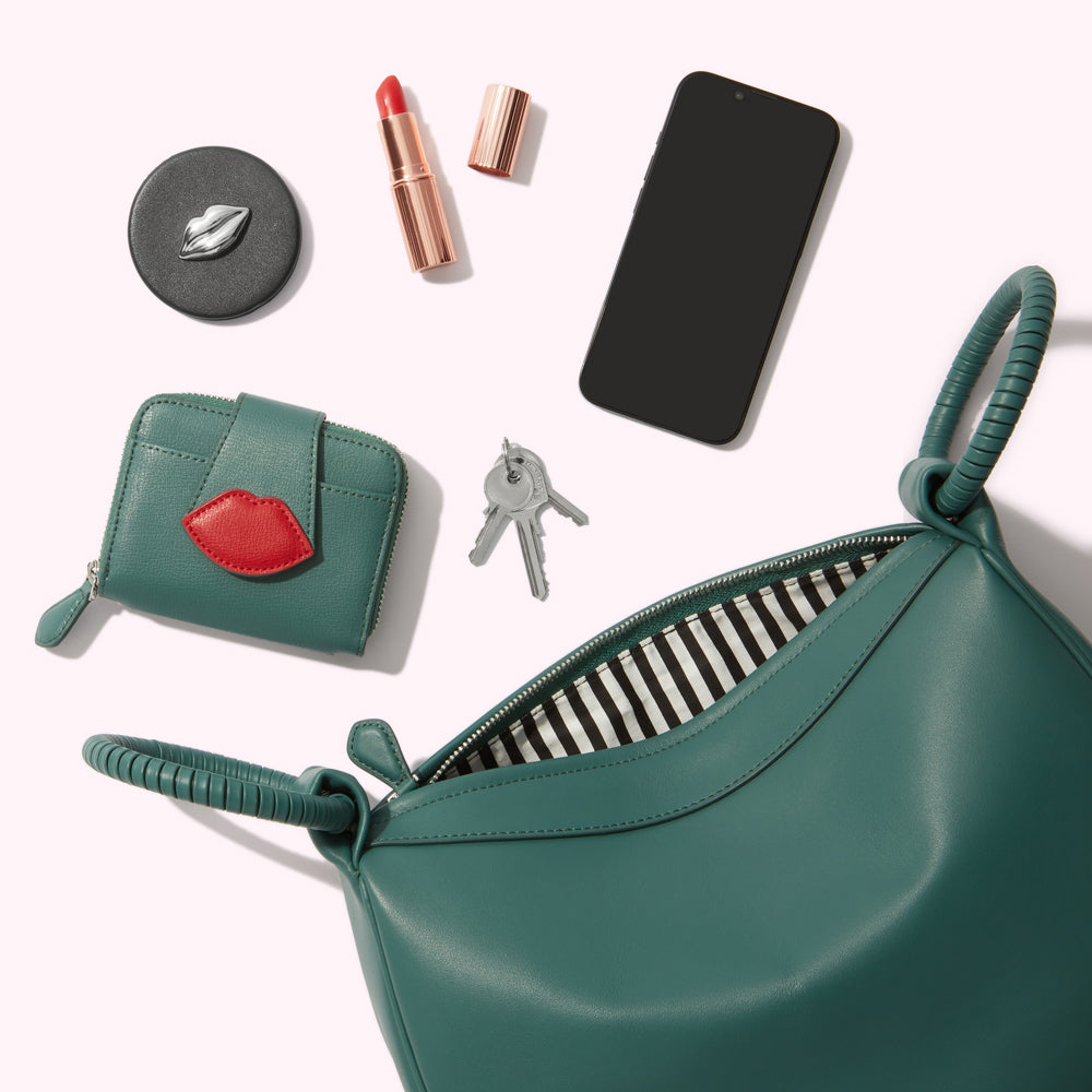 Teal leather handbag open to reveal a black and white striped lining, alongside a lipstick, compact mirror, keys and smartphone on a white background.