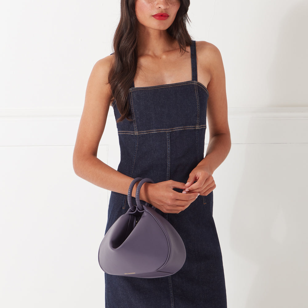 Woman in a denim dress holding a purple handbag.