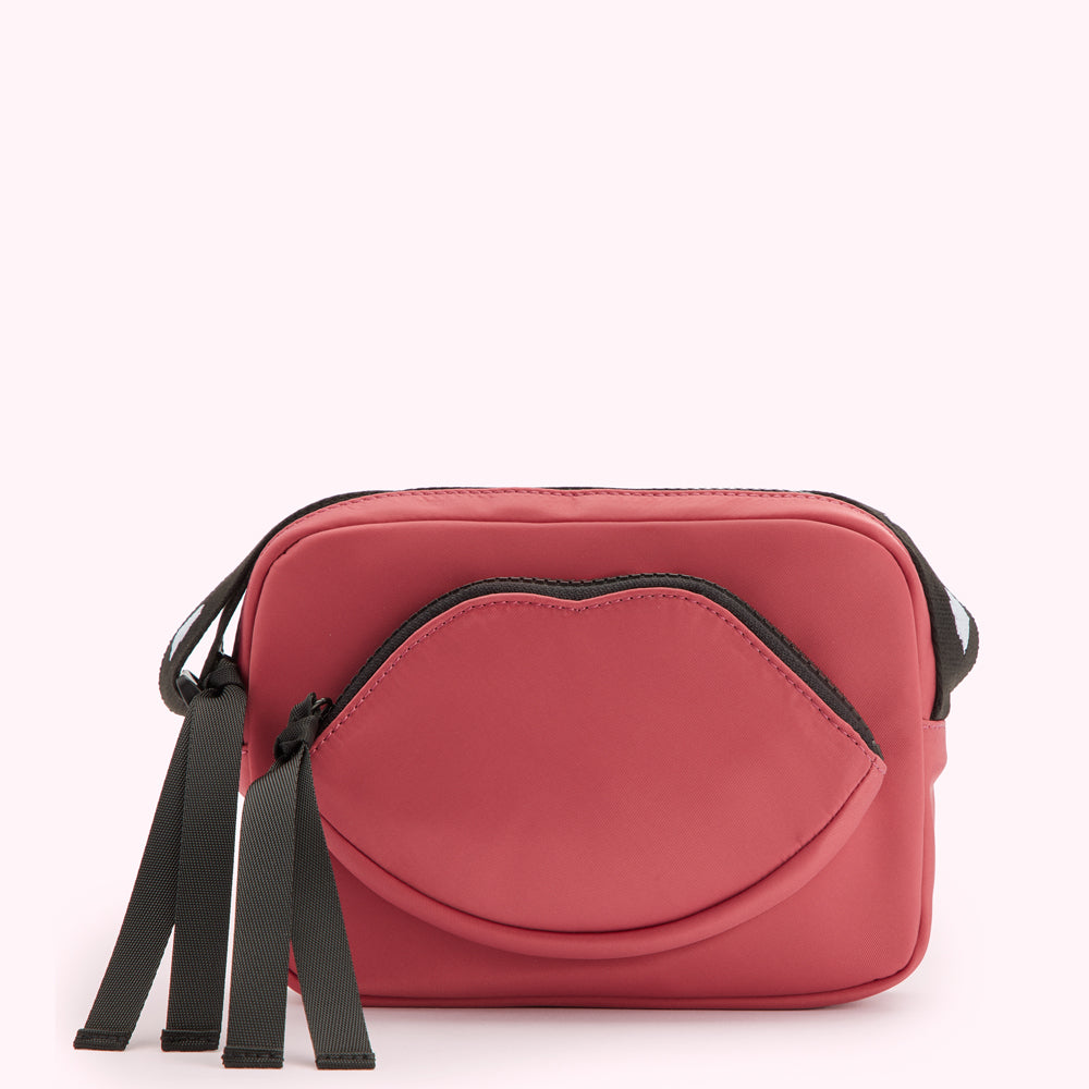 Dusty rose crossbody bag with a lip-shaped pocket and black straps.
