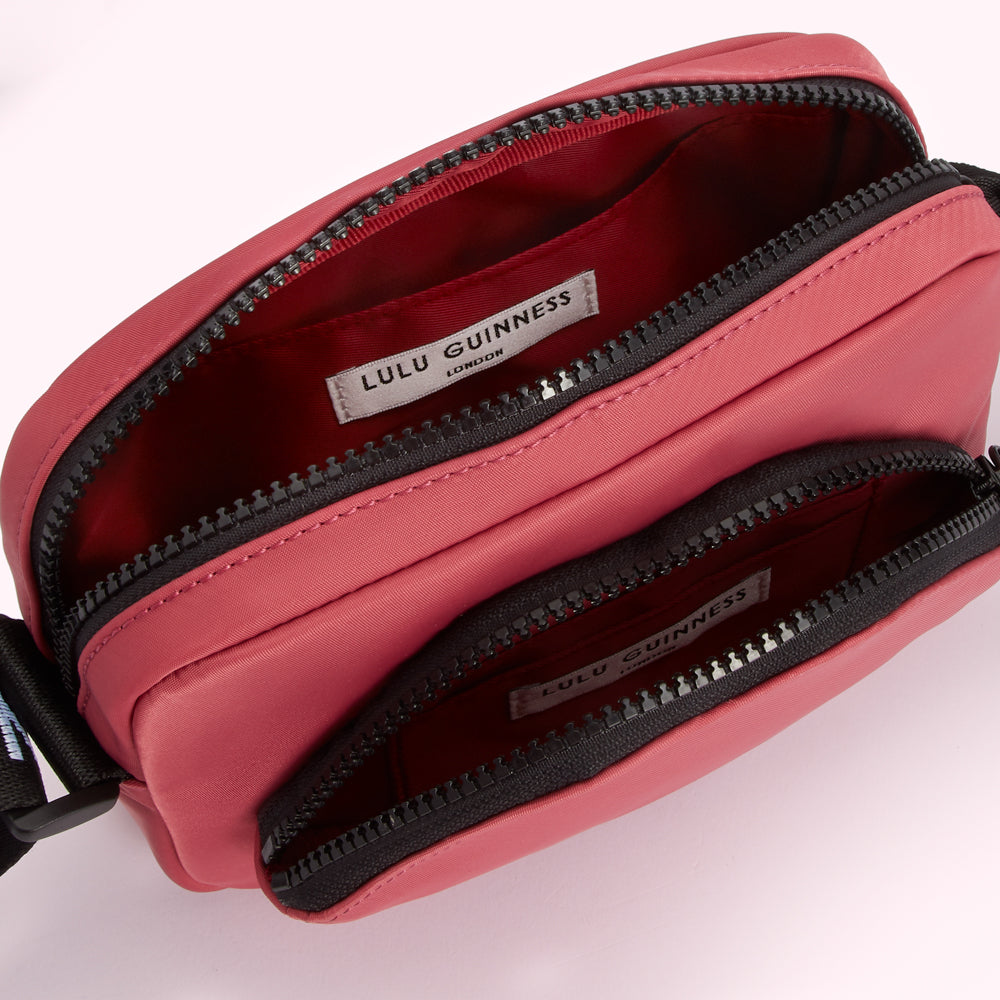 A coral pink Lulu Guinness crossbody bag with two zippered compartments, showing the inside of the bag.

