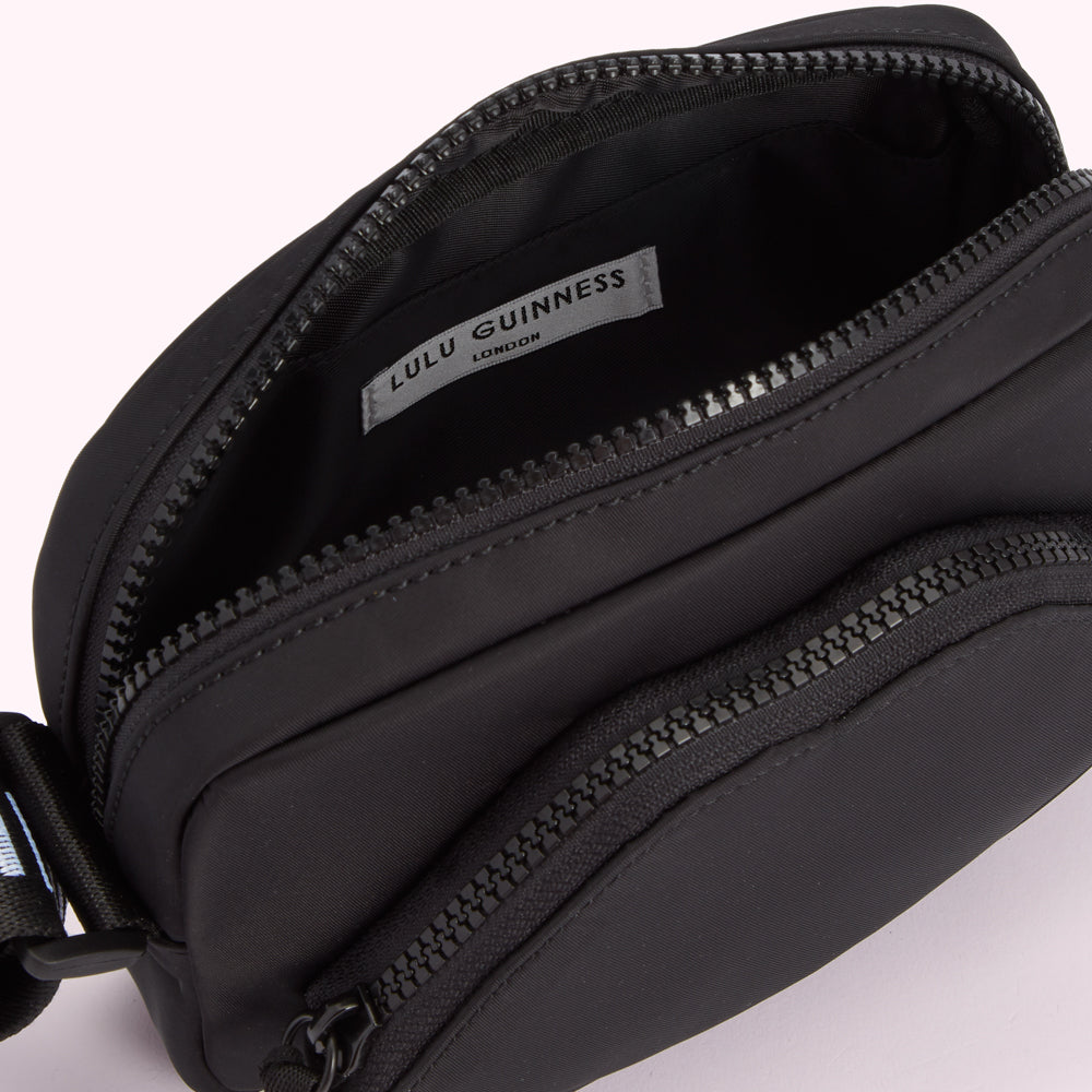 Close-up of the inside of a black Lulu Guinness London crossbody bag, showing the zippered compartments and brand label.

