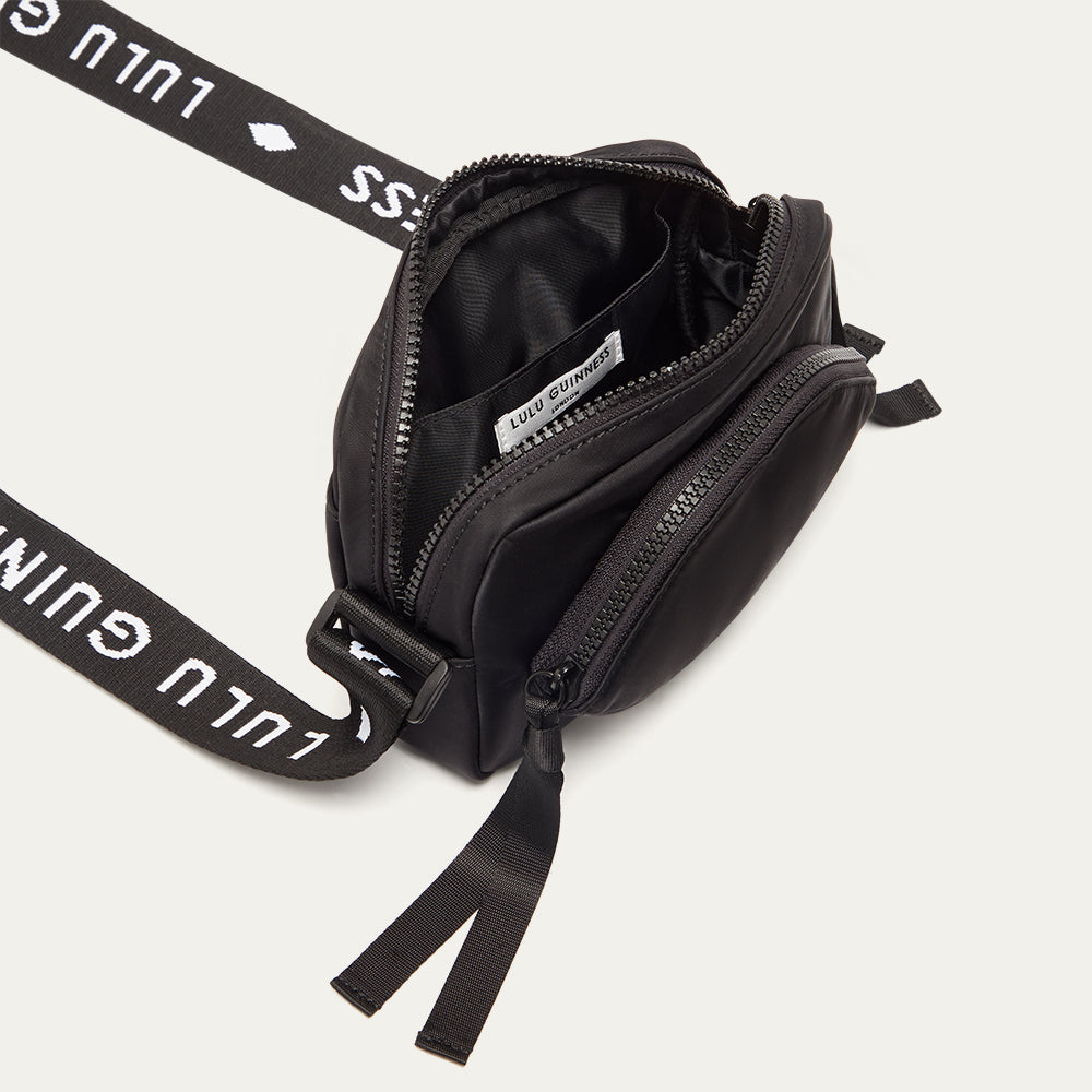 Black crossbody bag with a branded 'Lulu Guinness' strap open revealing a black lining on a white background