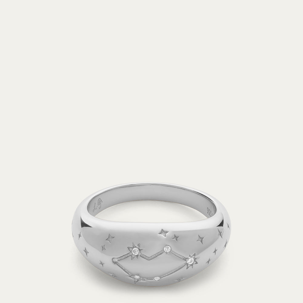 Silver domed ring with a engraved lip-shaped constellation, inset stones and star details on a off white background.
