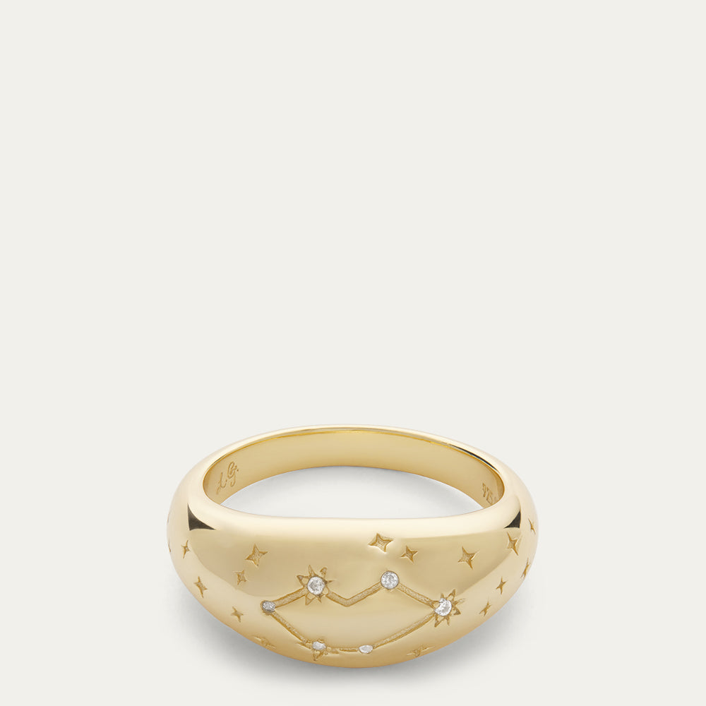 Gold dome shaped ring with a lip constellation and star engraved detailing on a off white background.