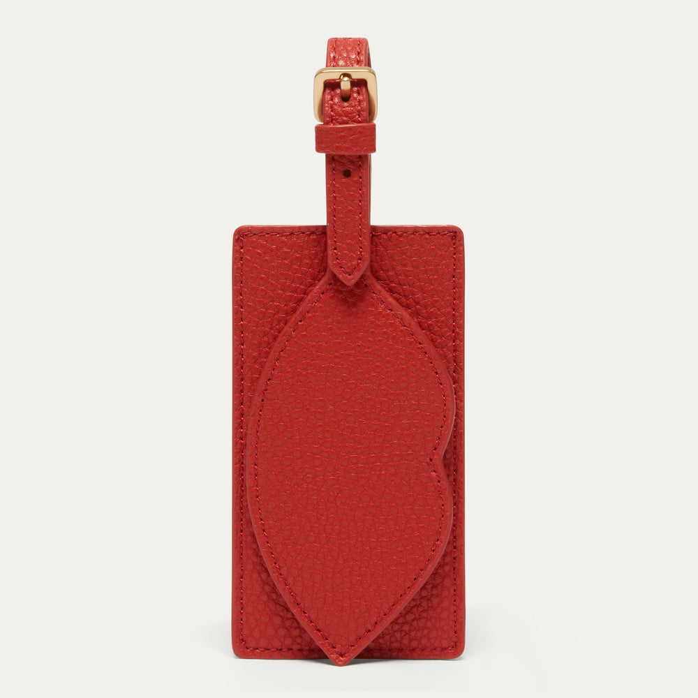 A red textured leather luggage tag with a matching strap and gold-tone buckle, displayed against a light off-white background.
