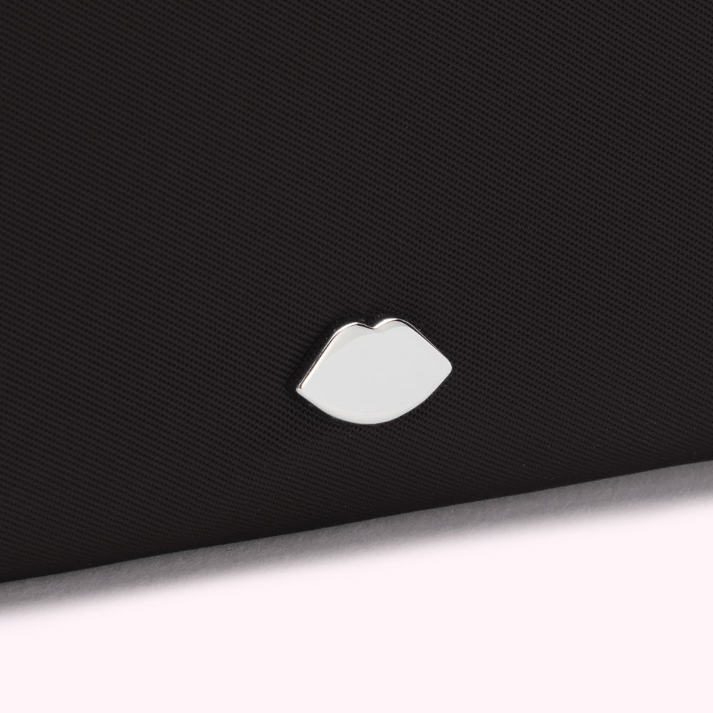 Close-up of a black textured surface with a silver lip-shaped emblem.
