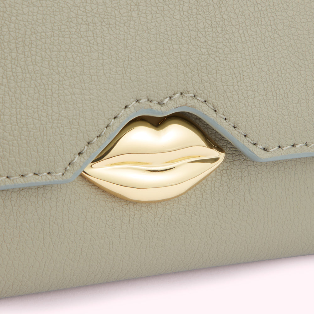 Close-up of a sage green leather wallet with a gold lip-shaped clasp.
