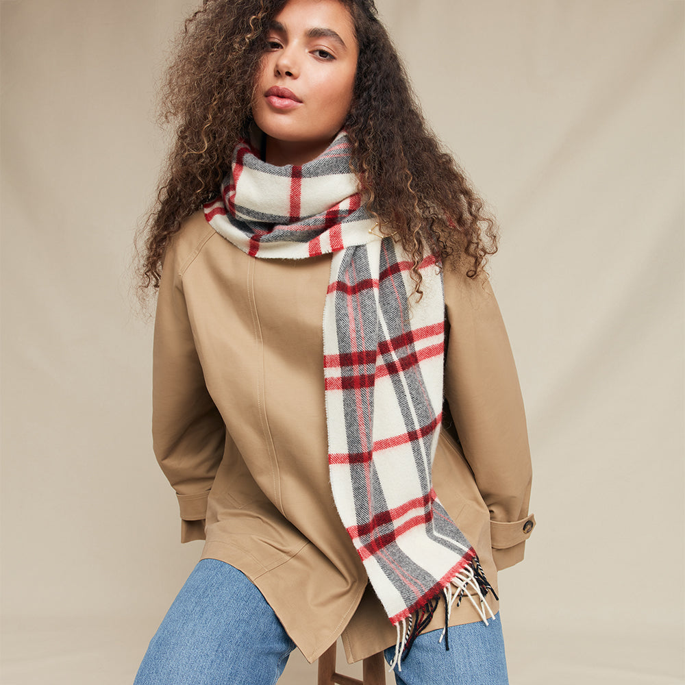 Woman wearing a beige coat and blue jeans with a plaid scarf against a beige background