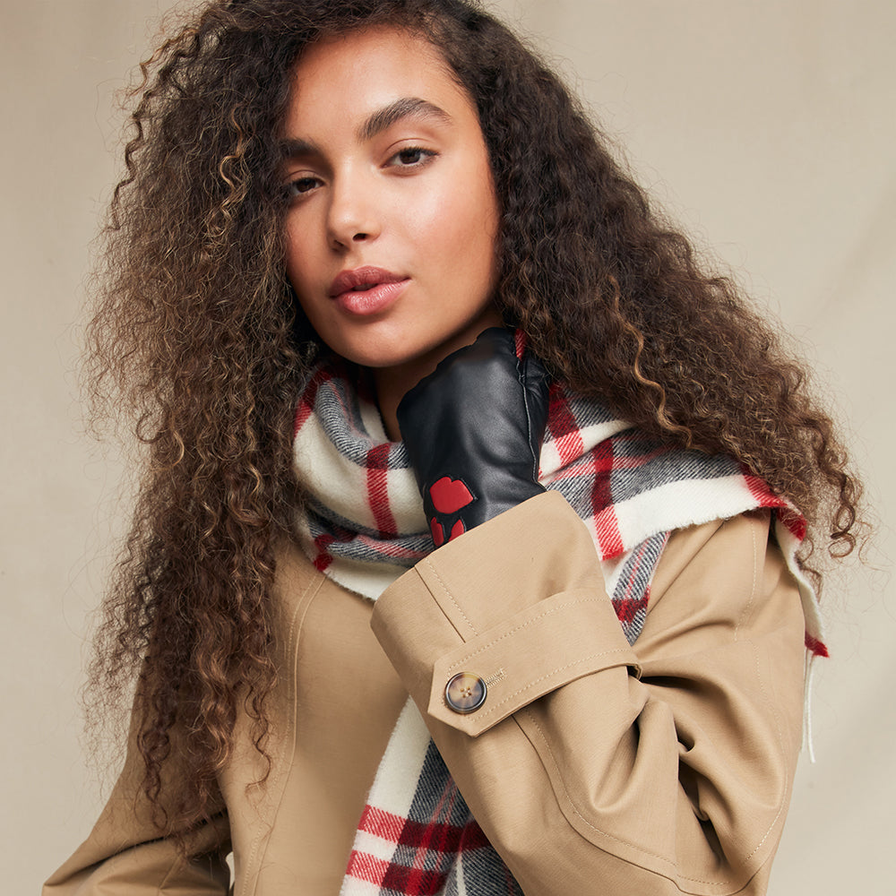 Woman wearing a beige coat, plaid scarf and black leather gloves against a neutral background