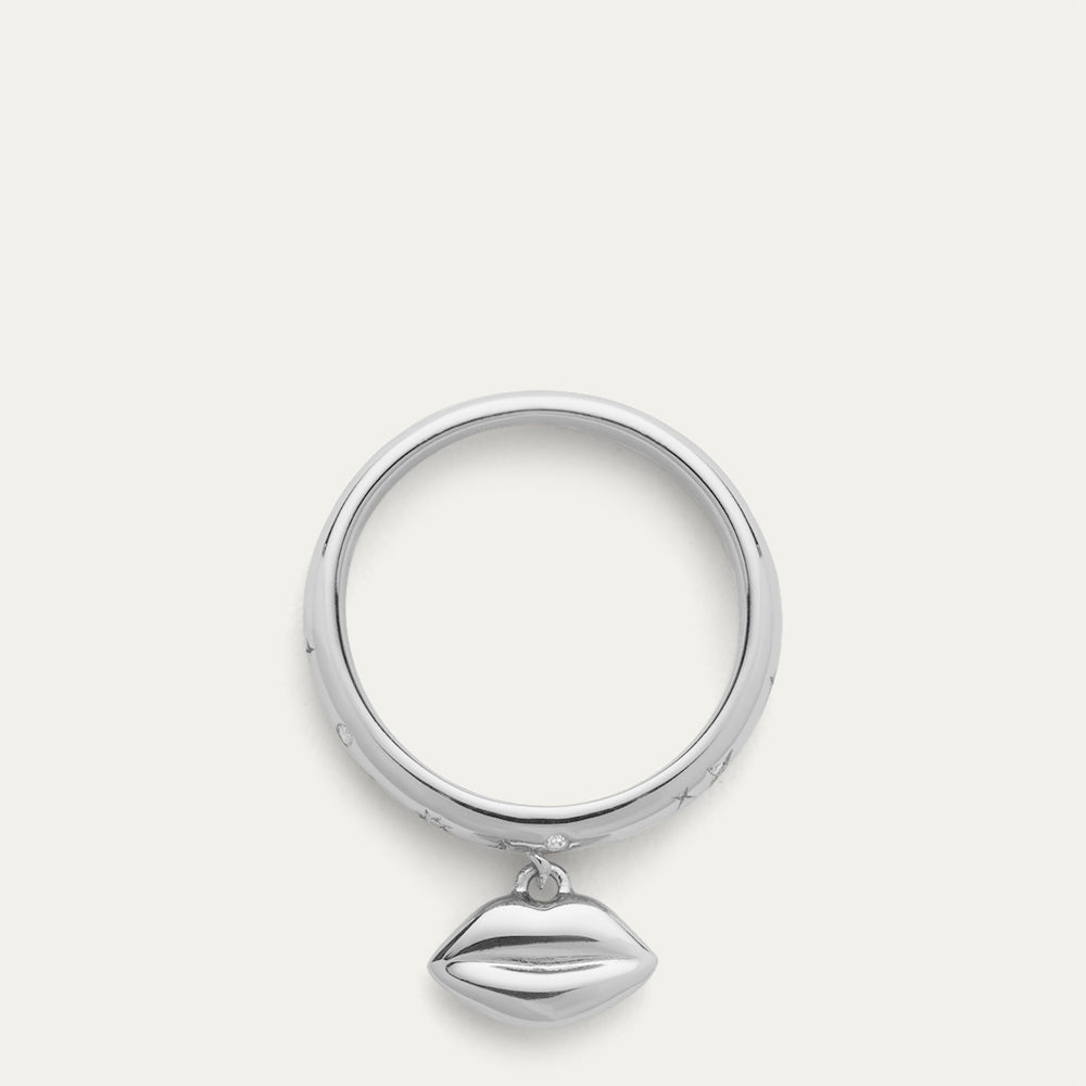 Silver ring with a lip-shaped pendant and inset stones on a off white background.