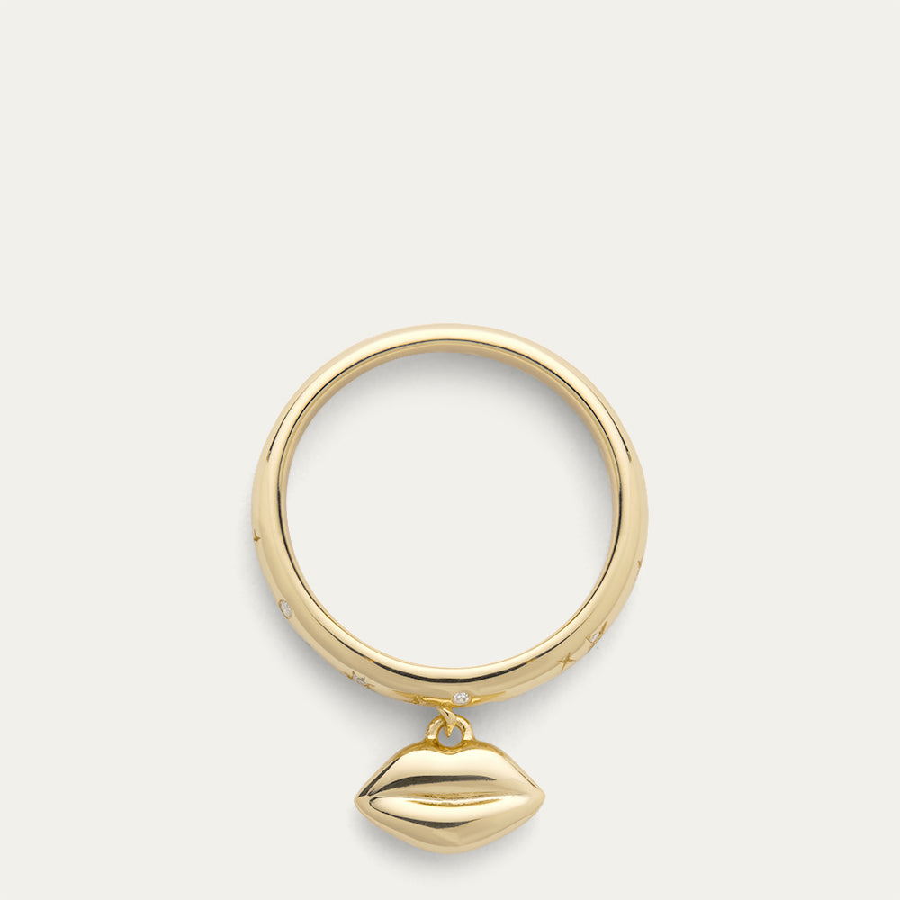Gold ring with lip shaped pendant and inset stones on a grey background.