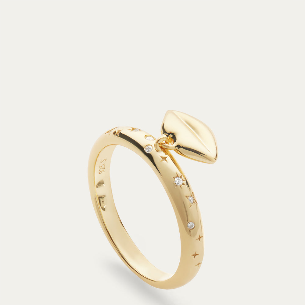 Gold ring with lip shaped pendant and inset stones on a grey background.