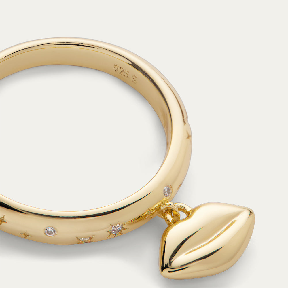 Close-up image of a gold ring with lip shaped pendant and inset stones on a grey background.