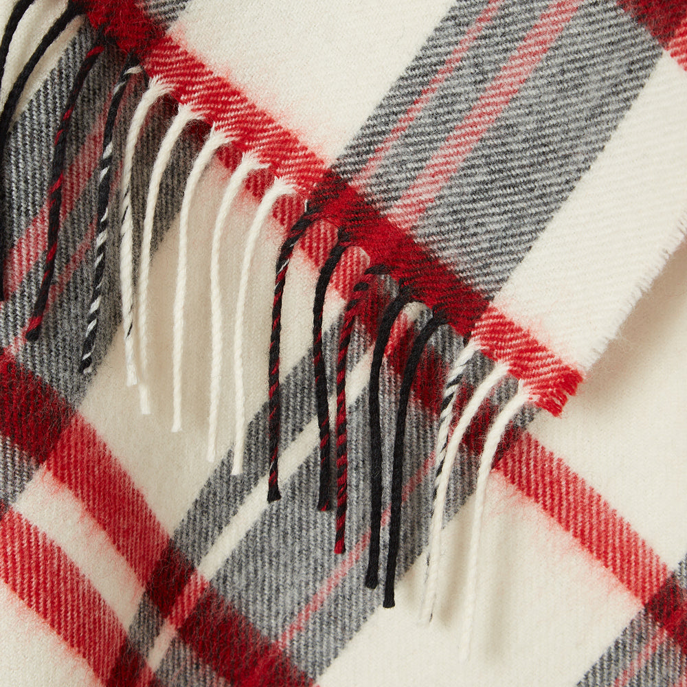 Close-up of a cream, red, and grey plaid or tartan scarf with fringed edges.
