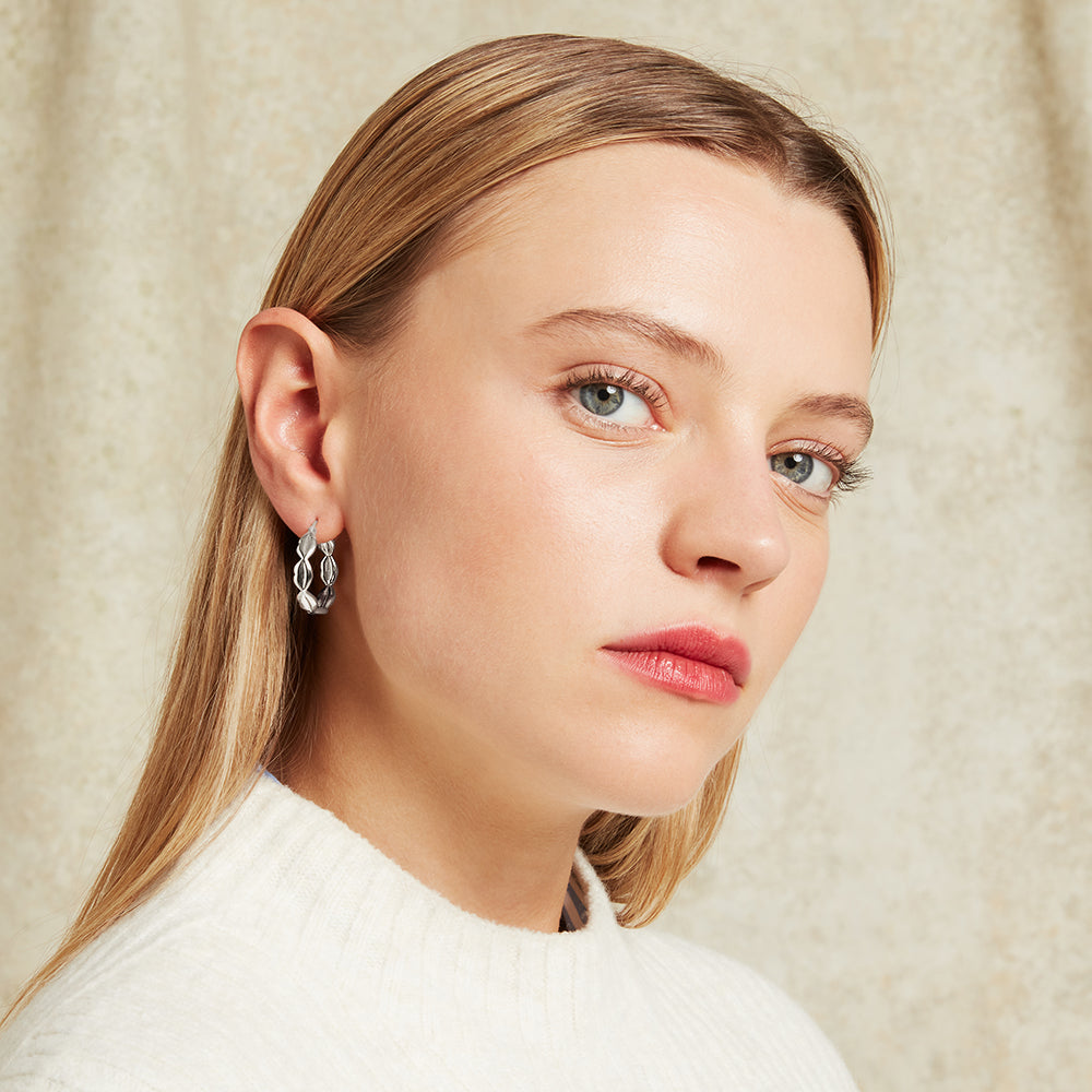 Close-up of a woman wearing silver lip link hoop earrings with a neutral background