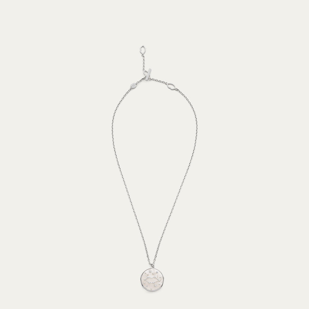 Silver necklace with a round pendant with a star and constellation design on a light gray background