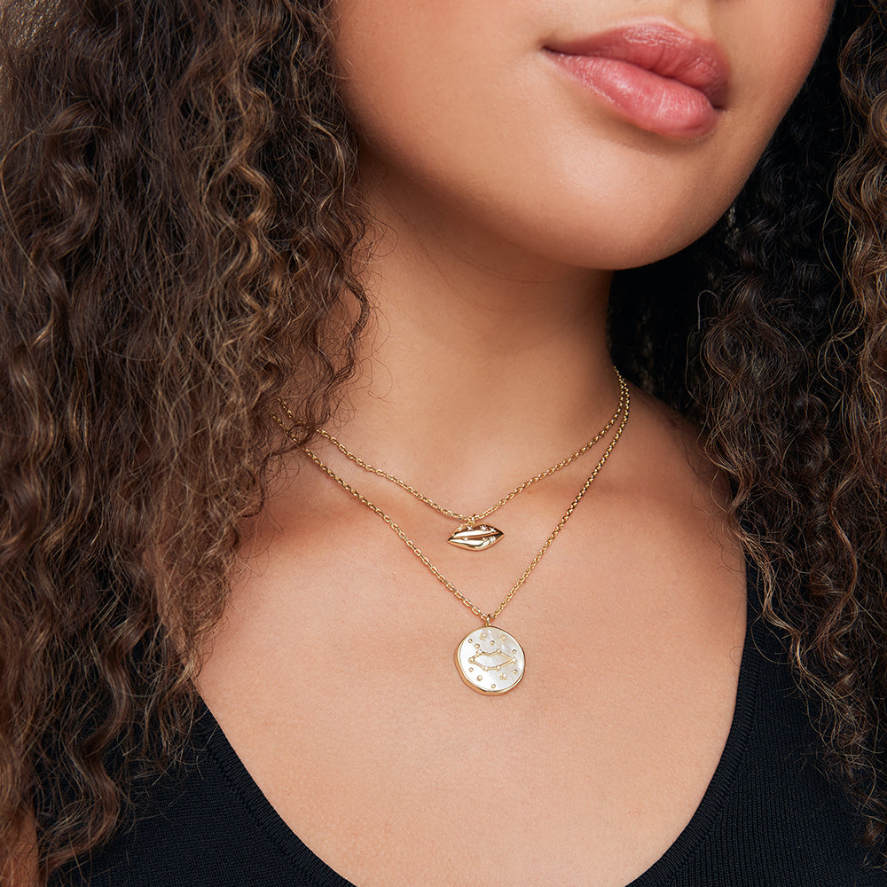 Close-up of a woman wearing two gold necklaces with pendants.