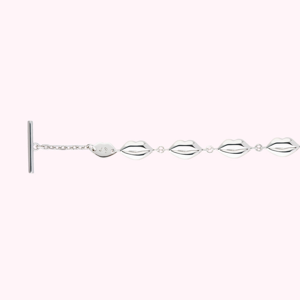 Silver lip-shaped charm bracelet on a pink background.