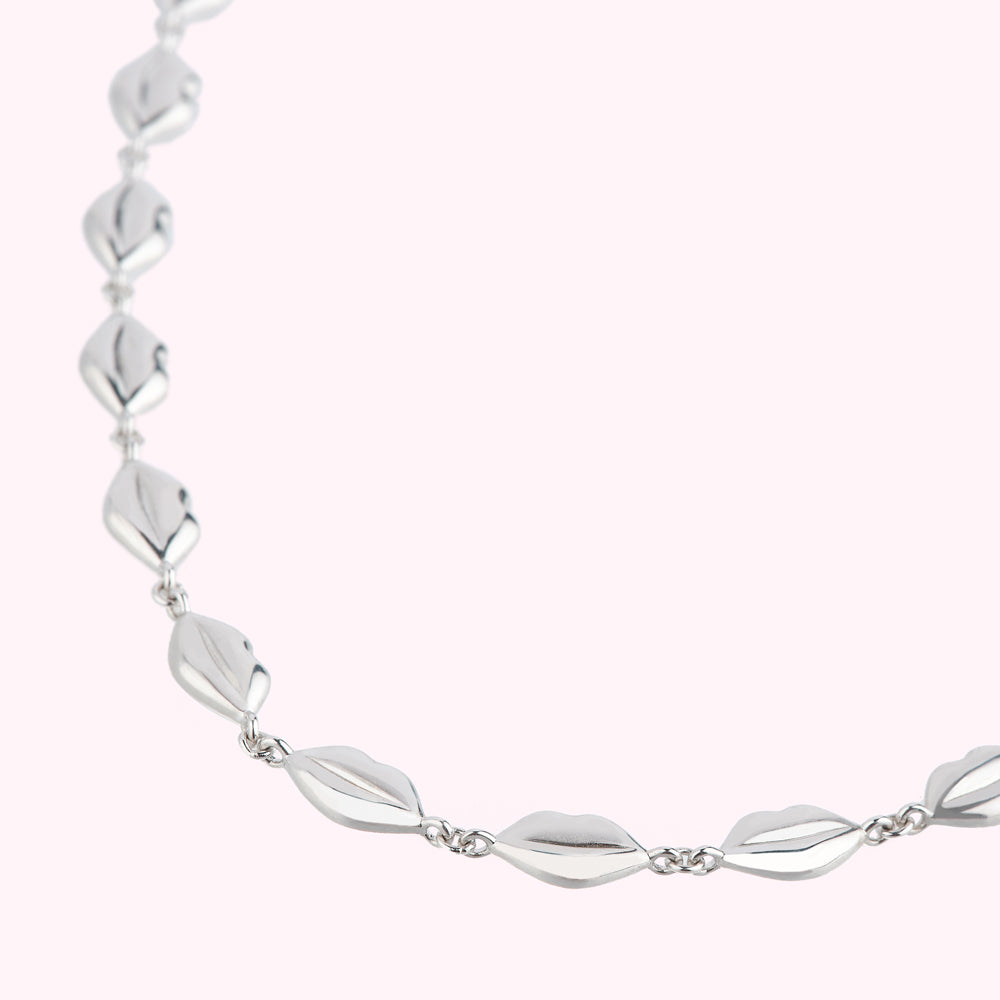 Silver necklace with lip-shaped pendants on a light pink background.
