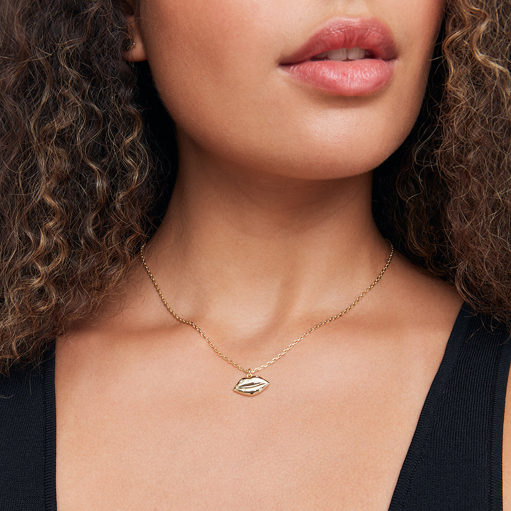 Close-up of a woman wearing a gold necklace with a lip-shaped pendant.
