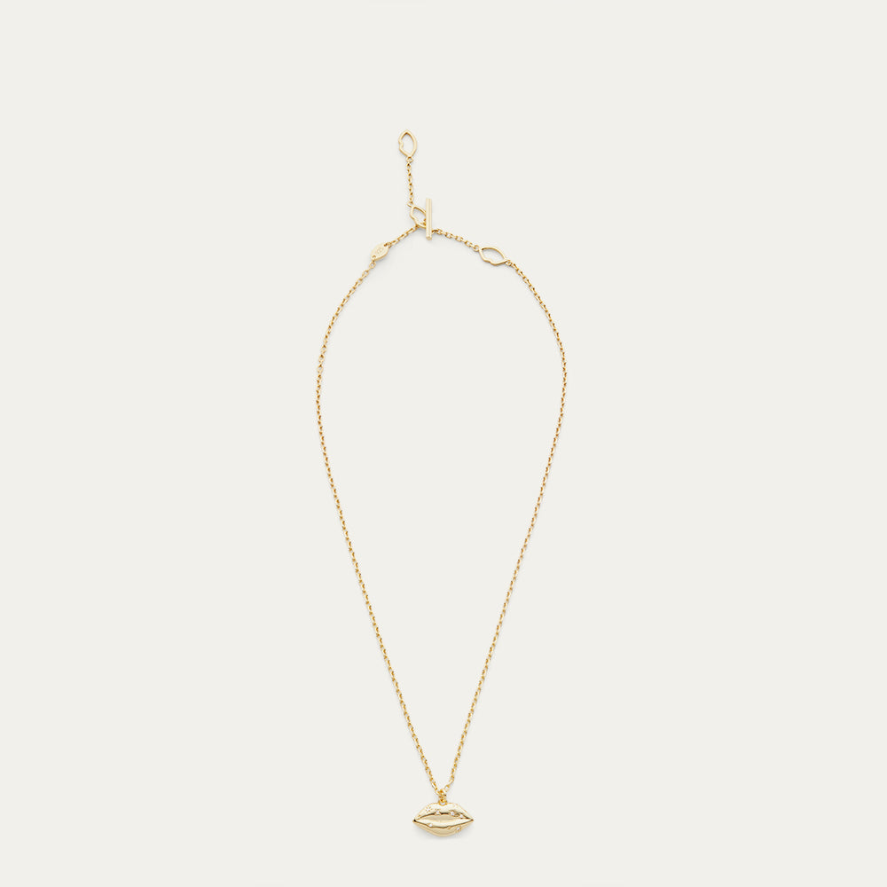 Gold necklace with a lip-shaped pendant with a crystal design on a light beige background