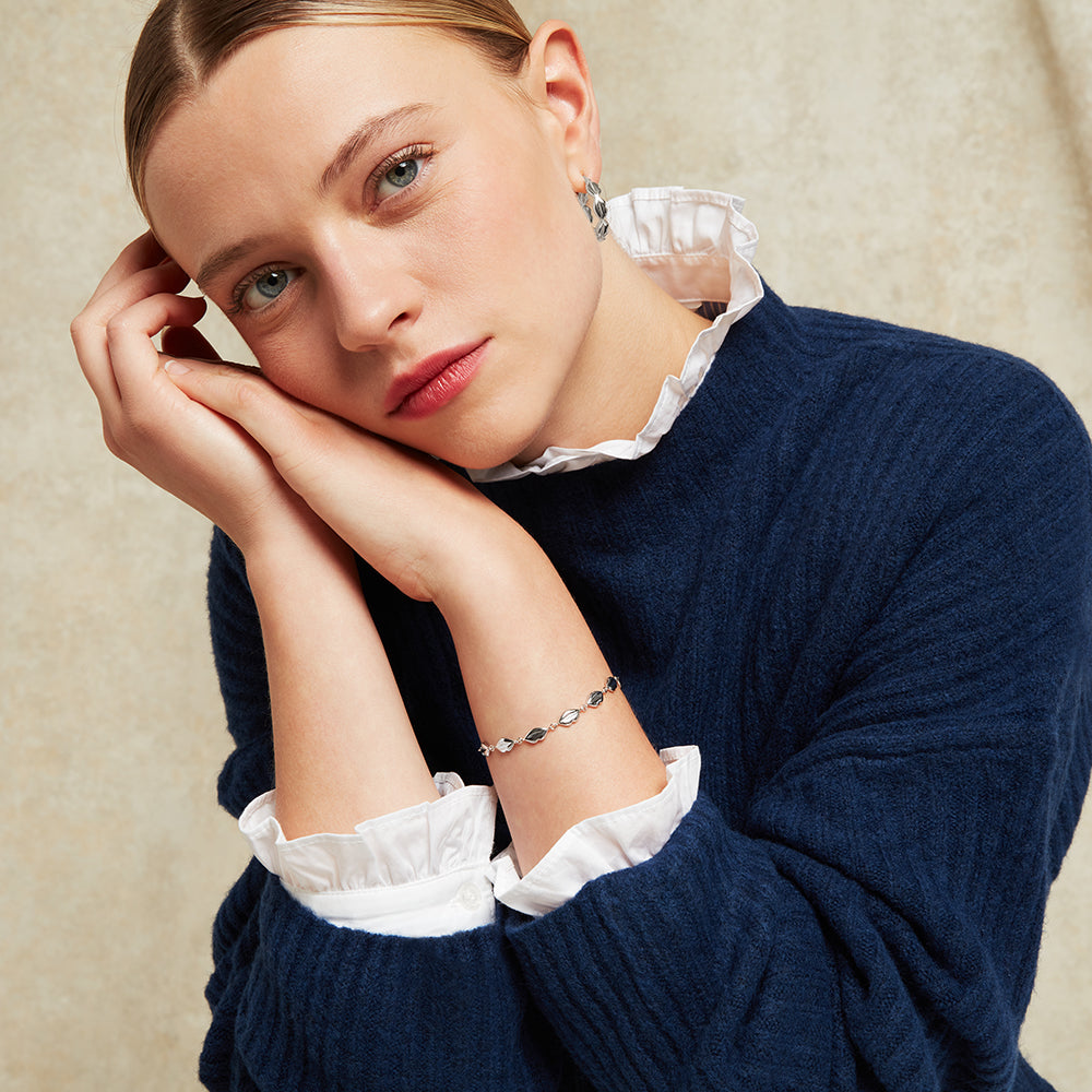 Woman in a navy blue sweater with white cuffs and collar wearing a silver lip link bracelet against a beige background