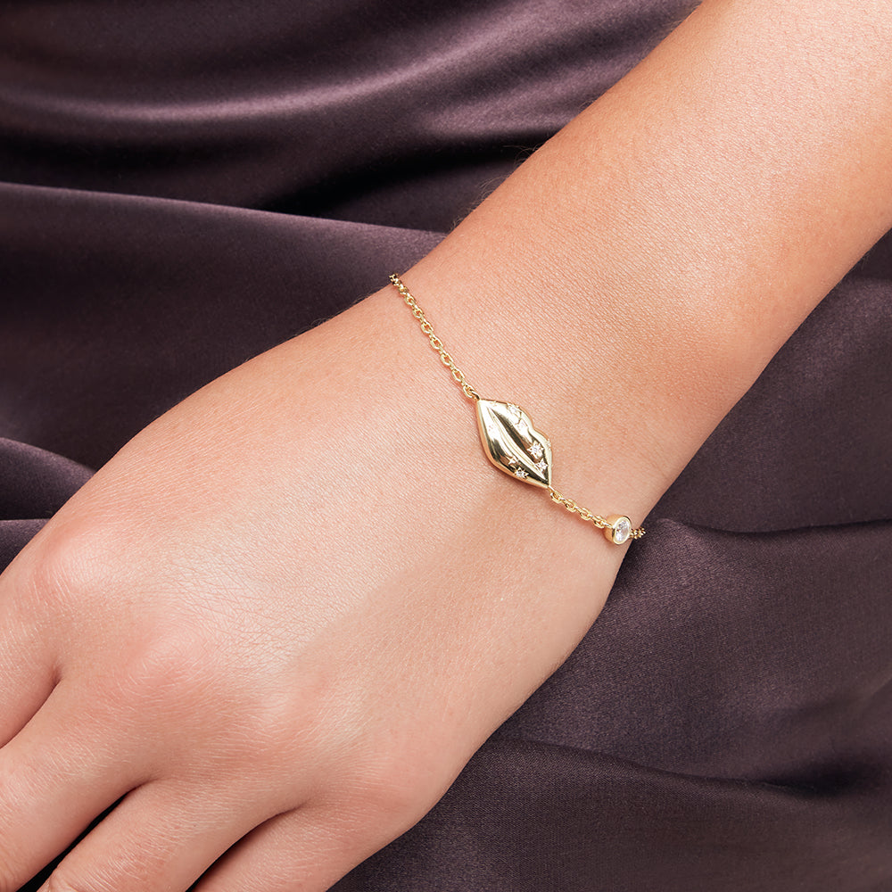Gold bracelet with lip charm and inset crystals on a light gray background