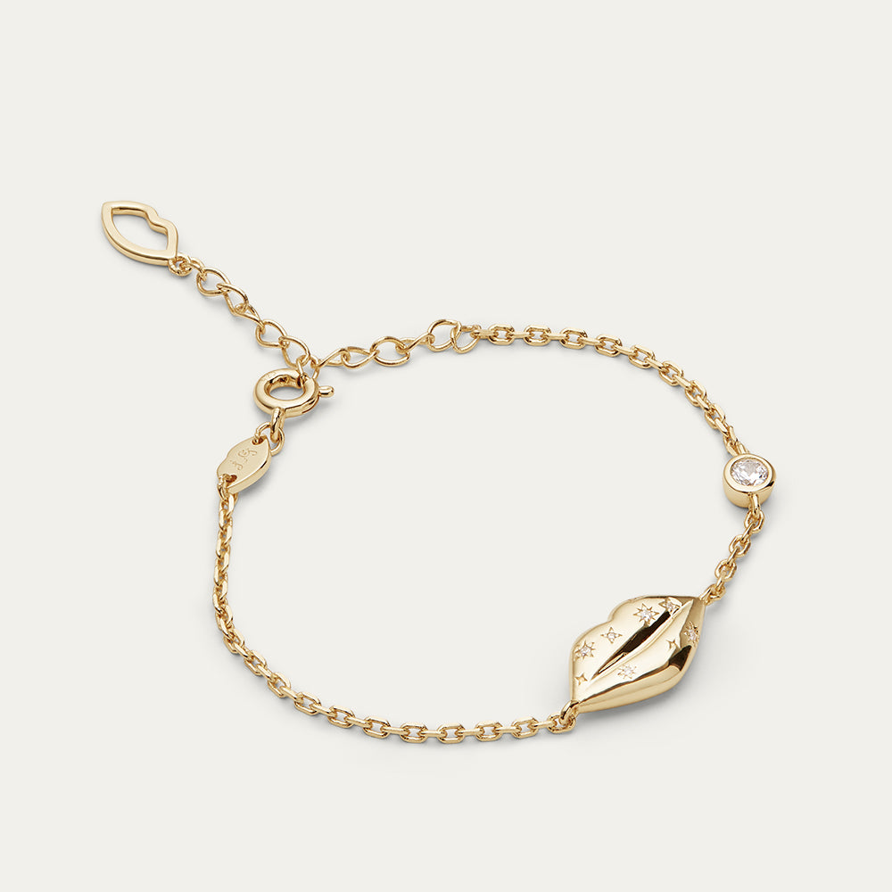 Gold bracelet with lip charm and inset crystals on a light gray background