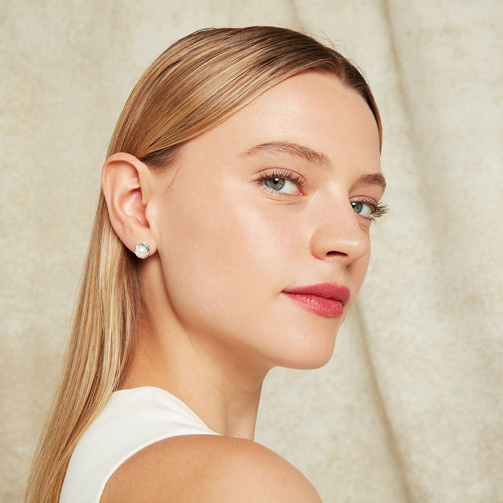 Woman wearing a silver stud earring with pearls against a neutral background