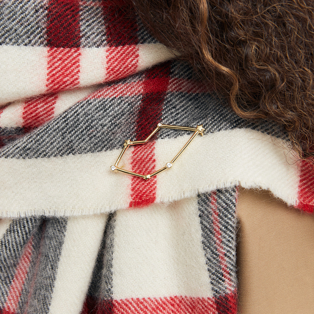 A gold lip shaped constellation brooch with star and crystal details pinned onto a plaid check scarf.