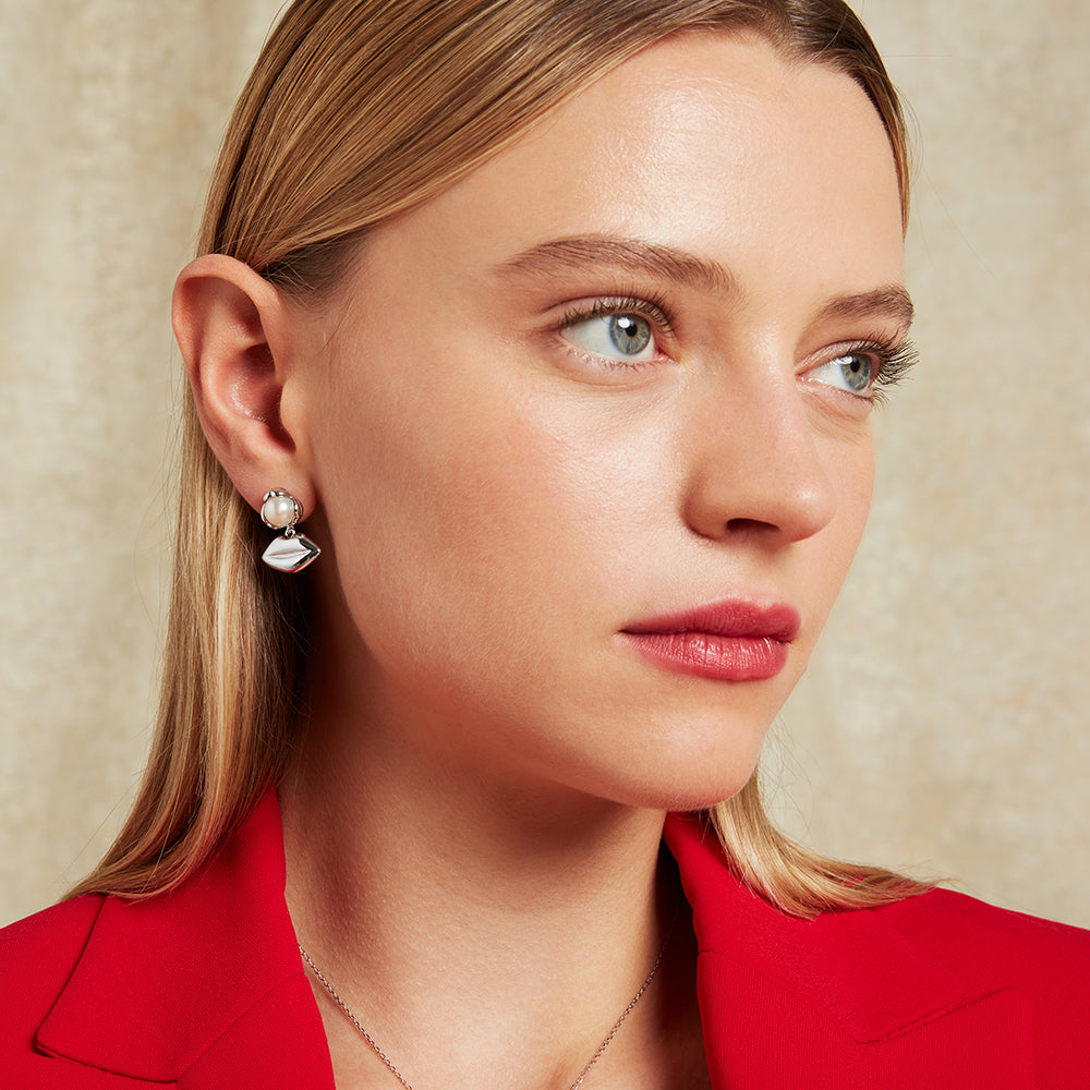 Close-up of a woman wearing silver pearl lip drop earrings with a neutral background