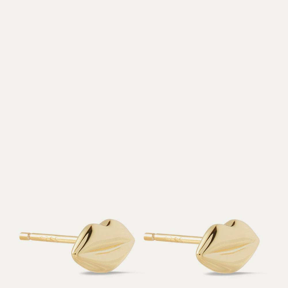 Gold lip-shaped earrings on a light beige background