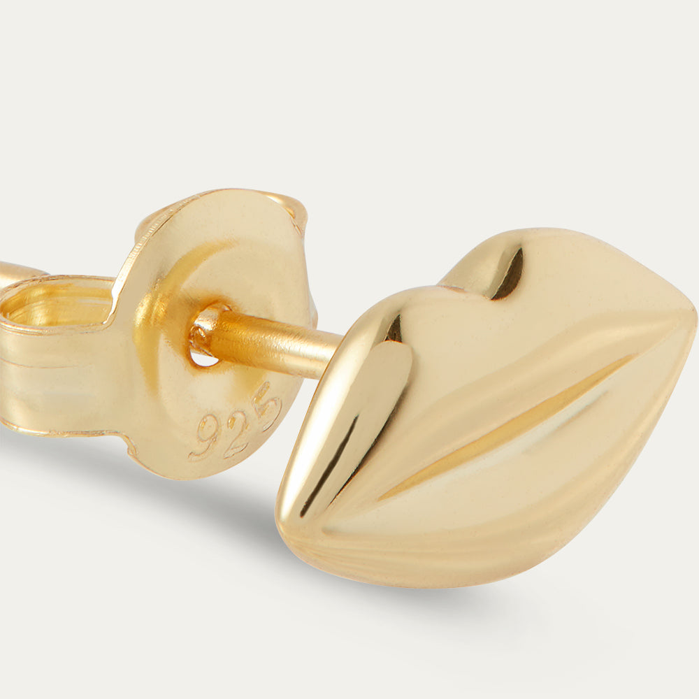 Gold lip-shaped earring on a light gray background