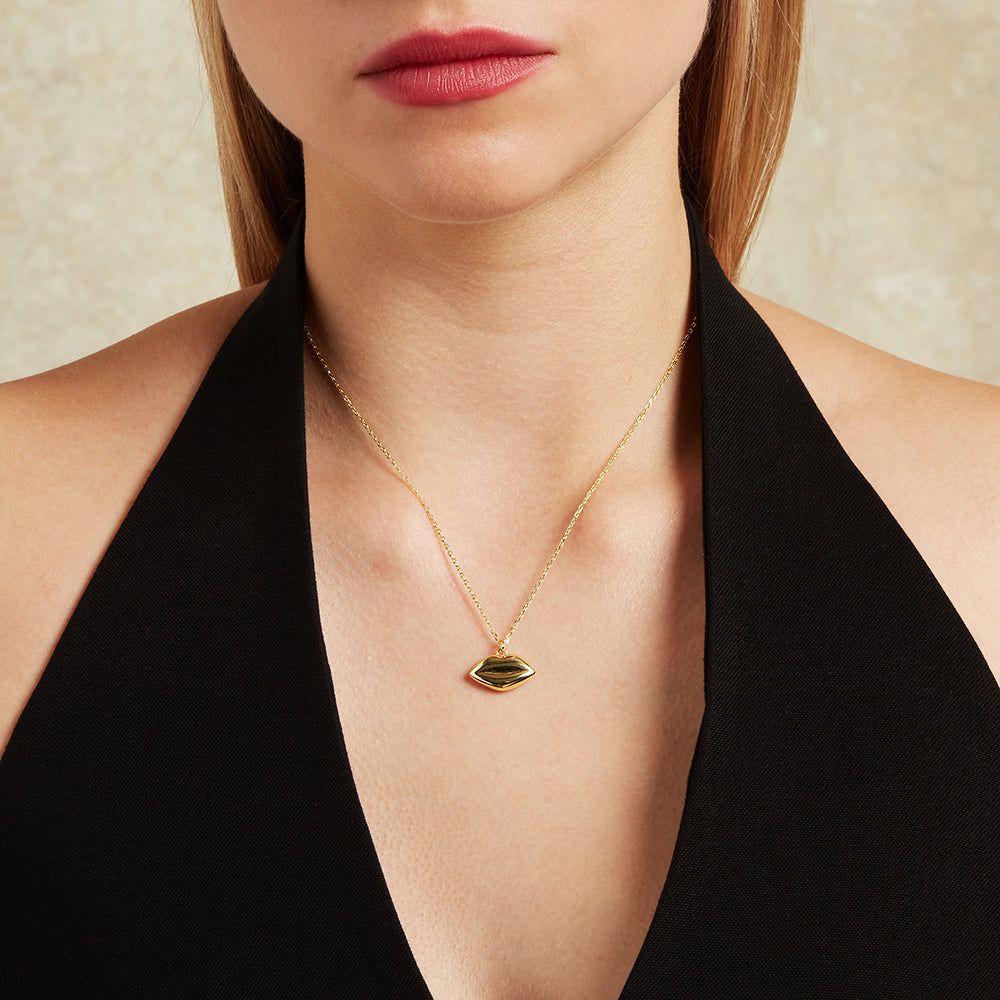 Gold necklace with a lip-shaped pendant worn by a person in a black top.