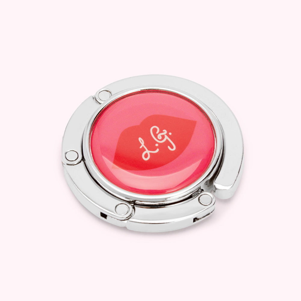 Silver handbag hook with a red circular design featuring a lip print and the letters L.G.J.