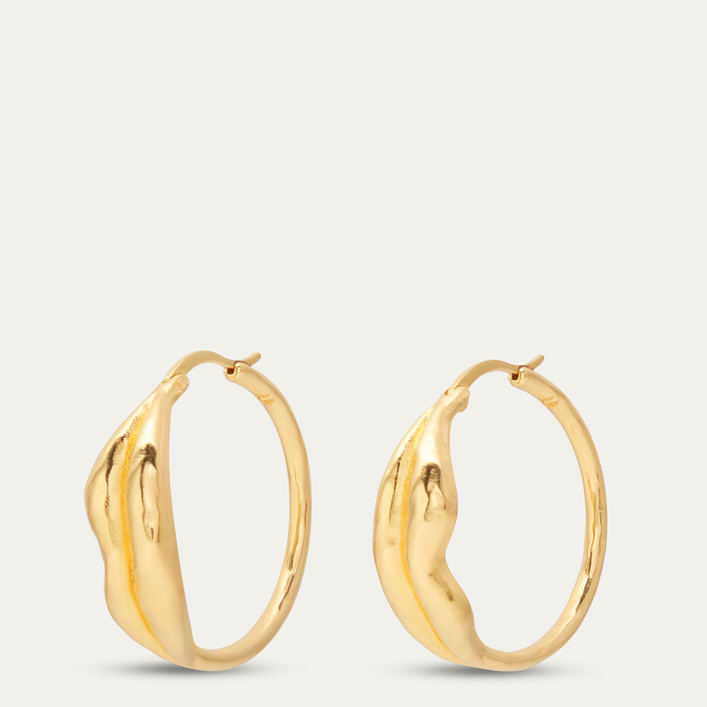 A pair of polished gold hoop earrings with a textured, organic lip design, displayed against a solid light gray background.