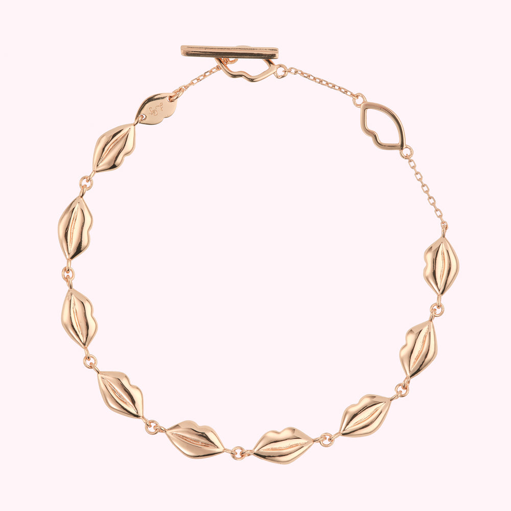 Rose gold lip-shaped charm bracelet on white background.
