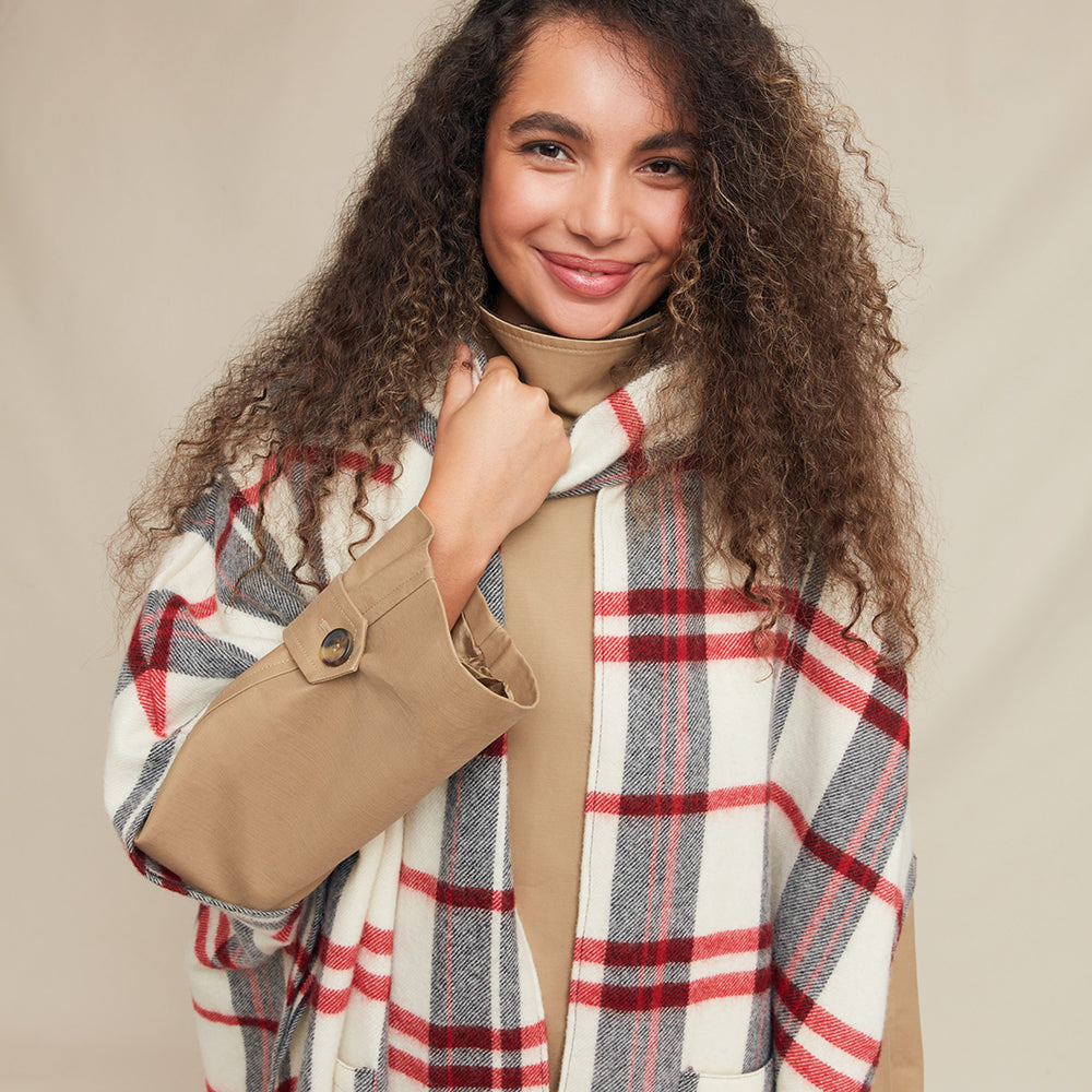 Woman wearing a beige coat and plaid over jacket against a beige background