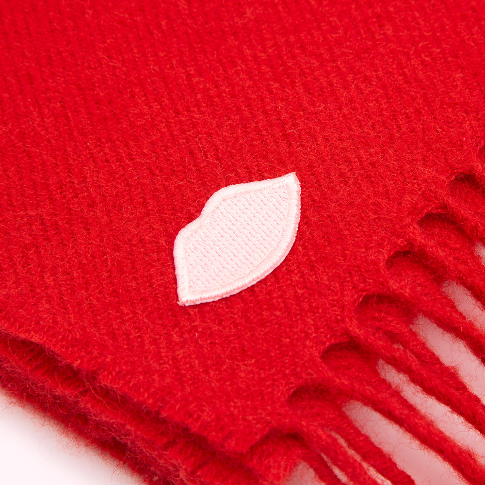 Close-up of a red knit scarf with a small, embroidered pink lip design.
