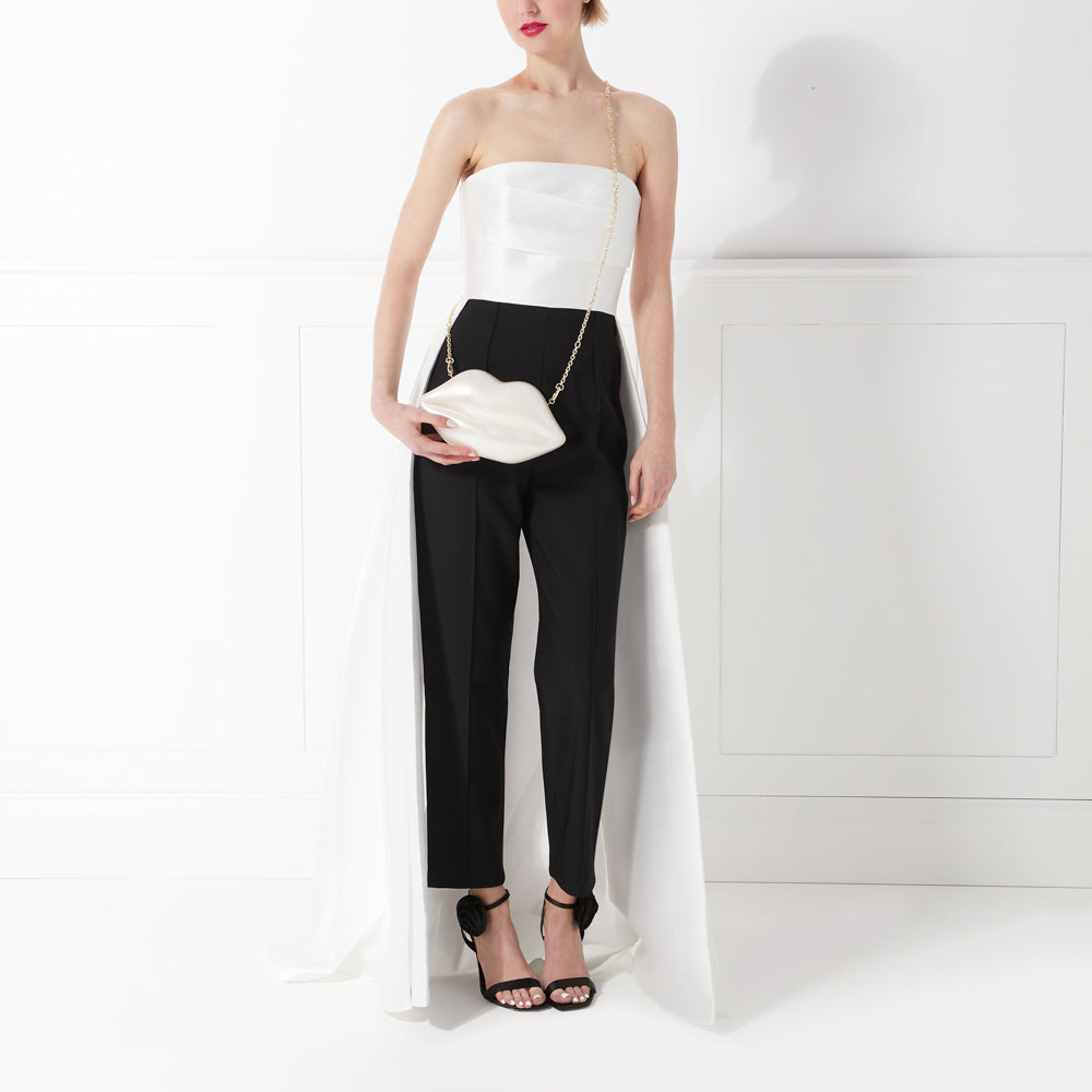 Woman in black pants and white strapless top with long white overlay and white lip-shaped purse.

