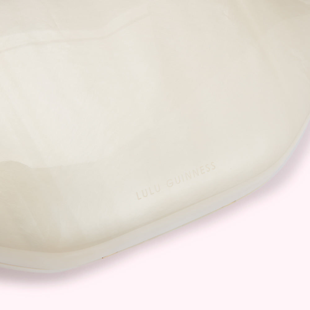Close-up of a cream-colored Lulu Guinness bag showing the brand name embossed on the bag.
